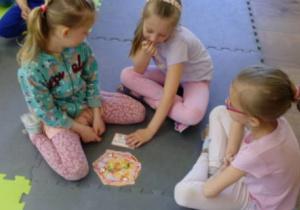 Trzy dziewczynki na dywanie piankowym układają składniki na włoskiej pizzy wg zamówienia